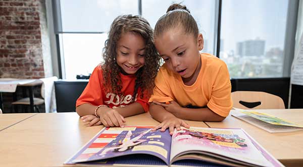 children sitting at a desk reading a book together